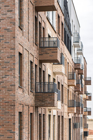 Modern brick building with multiple balconies with metal railings and windows, featuring a cloudy sky background, concept of urban architectureの写真素材