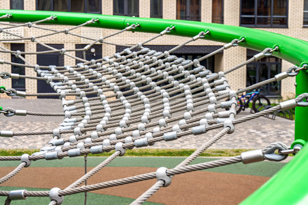Sturdy rope climbing net with metal fasteners on a green playground structure, set against an urban...
