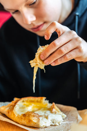 Boy tearing off cheesy bread from khachapuri with egg, close-up view, concept of traditional Georgian cuisineの写真素材