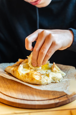 Boy tearing off cheesy bread from khachapuri with egg, close-up view, concept of traditional Georgian cuisineの写真素材