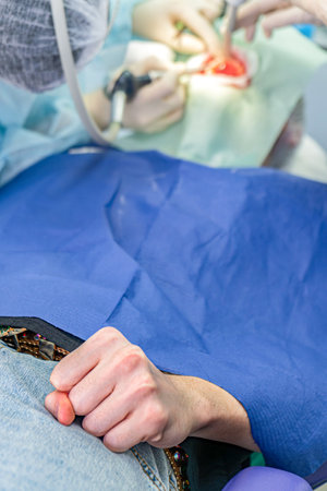 Patient anxiously clenches their fist in fear while receiving dental treatment at a clinic while dental team is focused on the task at handの写真素材