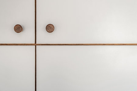 Sleek white cabinet facades of wooden closet featuring wooden knobs detailed close view as modern design backdropの写真素材