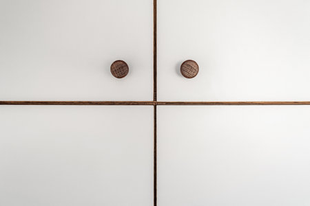 Sleek white cabinet facades of wooden closet featuring wooden knobs detailed close view as modern design backdropの写真素材