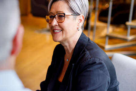 Smiling caucasian mature businesswoman with short hair wearing eyeglasses looking away while sitting...