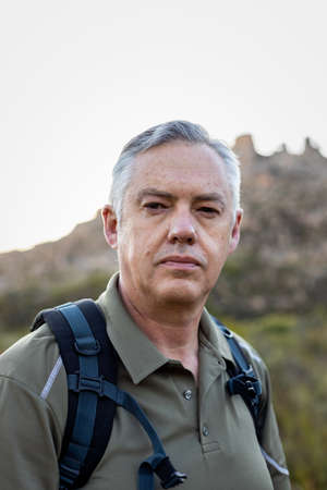 Close-up portrait of confident caucasian mature male hiker with backpack trekking alone against...