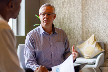 Serious mature male professional wearing eyeglasses explaining business strategy to young...