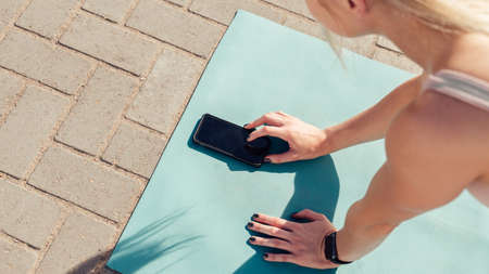High angle cropped hands of caucasian young woman using mobile phone on yoga mat while exercising...