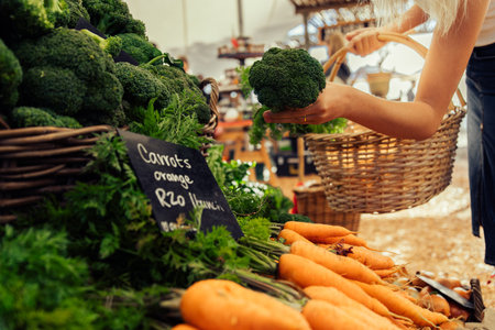 Cropped hands of young caucasian woman holding wicker basket and buying fresh broccoli at farmers marketの写真素材