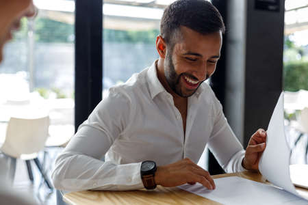 Bearded middle eastern young male professional smiling and analyzing performance report on desk in officeの写真素材