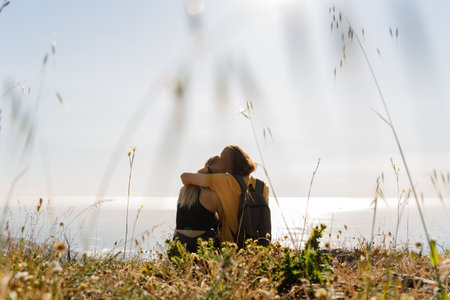 Rear view of romantic young couple looking at scenic seascape against clear sky while sitting on mountain during vacationの写真素材