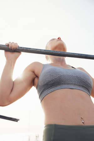 Low angle view of dedicated young female athlete practicing pull up exercise on rod against clear skyの写真素材