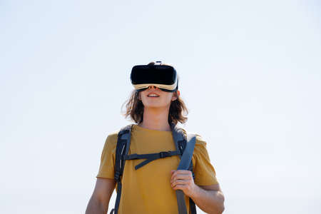Low angle view of young male wanderlust watching through virtual reality simulator against clear sky...