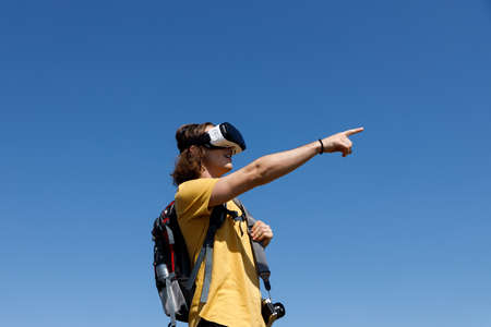 Low angle view of excited young male hiker pointing while exploring nature through virtual reality simulator against clear blue skyの写真素材