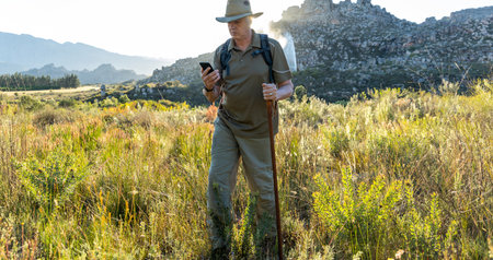Mature male hiker with backpack wearing hat and navigating direction over smartphone while enjoying...