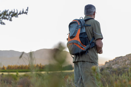 Full length of mature male wanderlust looking away and exploring nature while hiking with pole...