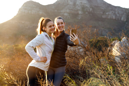 Female friends taking selfie while hiking early morning in the mountains at sunriseの写真素材