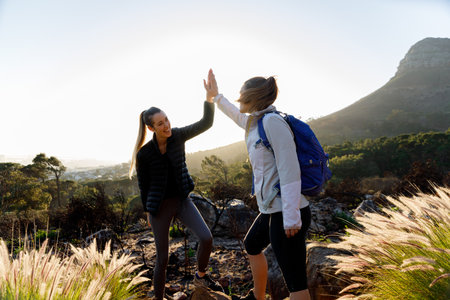 Happy caucasian young woman giving high five to female friend while hiking together in woodland...