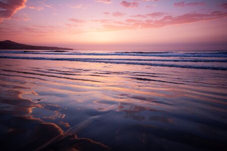 Calm ocean view at sunrise. Pink sky and reflections in the sand.の写真素材
