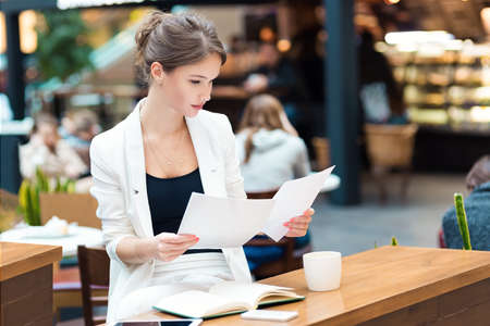 Young, beautiful girl in a white suit, sitting in the cafe at the business meetingの写真素材