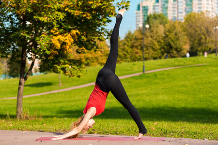Young beautiful girl is engaged in yoga, outdoors in a park in summer
