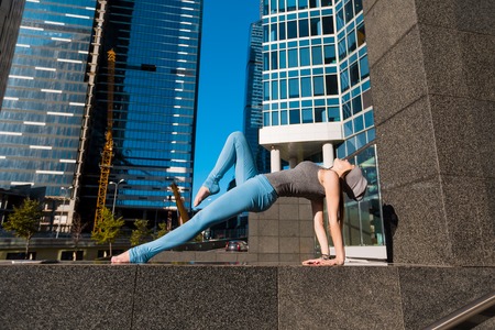 Young girl doing yoga outdoors in a city on the background of skyscrapers