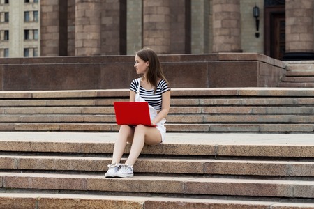 Young woman with a laptop sitting on the stairs, near the universityの写真素材
