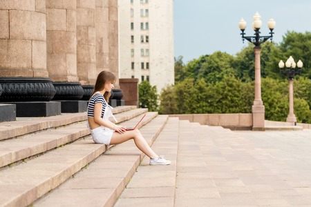 Young woman with a laptop sitting on the stairs, near the universityの写真素材