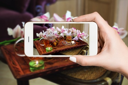 Woman photographing on smartphone, green tea set on a trayの写真素材
