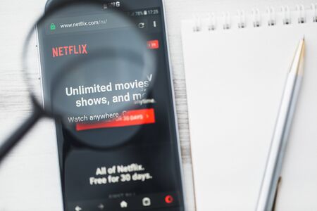 Los Angeles, California, USA - 3 April 2019: Netflix, Streaming media official website homepage under magnifying glass. Concept Film production, Netflix logo visible on tablet screen, smartphoneのeditorial素材