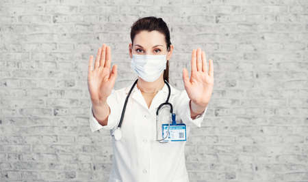 Doctor woman makes stopping hand gesture. Girl Doctor wearing protection face mask against covid-19....