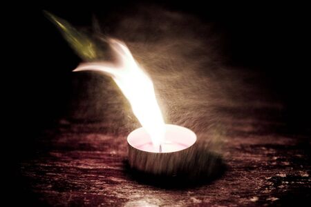 Small candle burning with a bright flame on a brown table.の写真素材