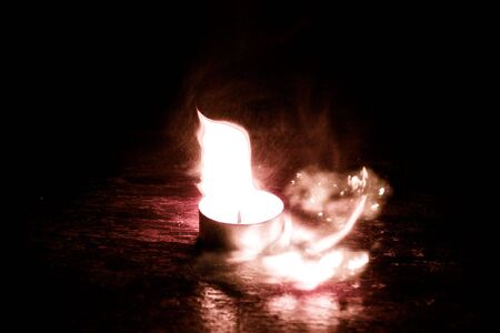 Small candle burning with a bright flame on a brown table.の写真素材