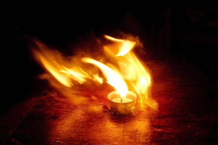 Small candle burning with a bright flame on a brown table.の写真素材