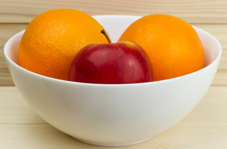 fresh juicy natural apples and oranges in a shiny white plate on wooden backgroundの写真素材