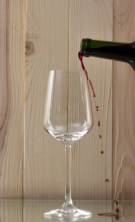 red wine being poured into a glass bottle of red wine with a brilliant glass oon a glass standの写真素材