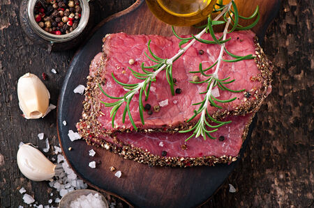 Raw beef steak with spices and a sprig of rosemaryの写真素材