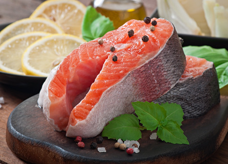 Fresh and raw steaks trout on a wooden cutting board with sliced lemon, basil and pepperの写真素材