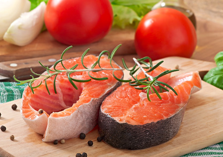 Fresh and raw steaks trout on a wooden cutting board with sliced lemon, rosemary and pepperの写真素材