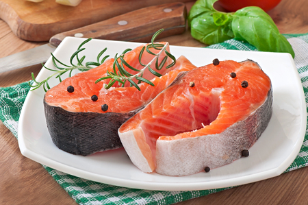 Fresh and raw steaks trout on a wooden cutting board with sliced lemon, rosemary and pepperの写真素材