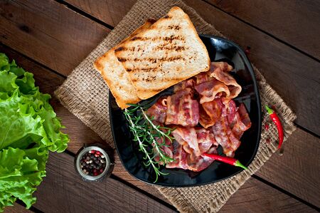 Fried bacon and toast on a black plate on a wooden backgroundの写真素材
