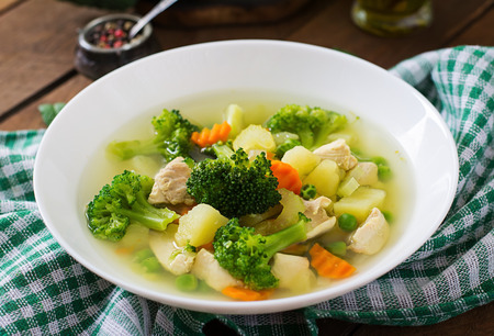 Chicken soup with broccoli, green peas, carrots and celery in a white bowl on a wooden background in rustic styleの写真素材