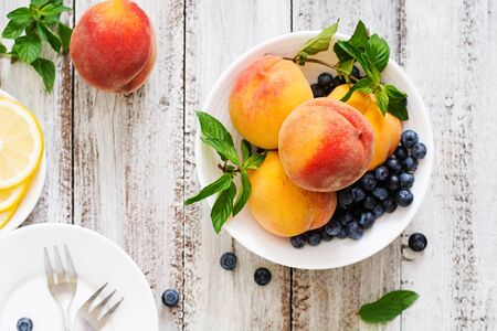 Fresh peaches and blueberries in bowl on a light wooden background in rustic style. Top viewの写真素材