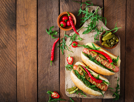 Hot dog with pickles, capers and arugula on wooden background. Top viewの写真素材