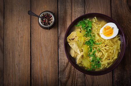 Noodle soup with chicken, celery and egg in a bowl on a old wooden background. Flat lay. Top view.の写真素材