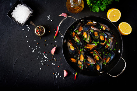 Mussels cooked in wine sauce with herbs in a frying pan on a black background. Flat lay. Top view.の写真素材