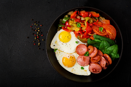 Breakfast. Fried eggs with sausage and vegetables in a frying pan on a black background in rustic style. Top viewの写真素材