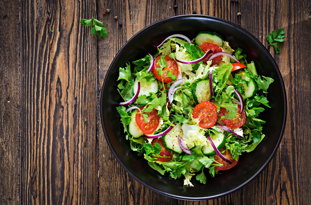 Salad from tomatoes, cucumber, red onions and lettuce leaves. Healthy summer vitamin menu. Vegan vegetable food. Vegetarian dinner table. Top view. Flat layの写真素材