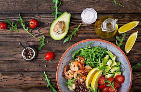 Delicious healthy Buddha bowl with shrimps, tomato, avocado, quinoa, lemon and arugula on the wooden table. Healthy food. Top view. Flat lay.の写真素材