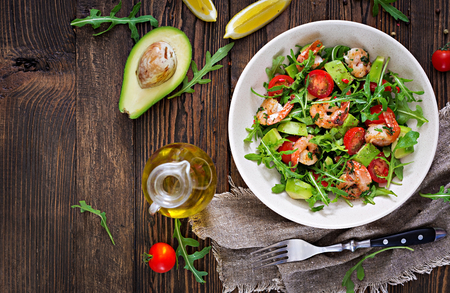 Fresh salad bowl with shrimp, tomato, avocado and arugula on wooden background close up. Healthy food. Clean eating. Top view. Flat lay.の写真素材