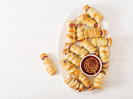 Scary sausage mummies in dough with funny eyes on table. Funny decoration. Halloween food. Top view. Flat layの写真素材
